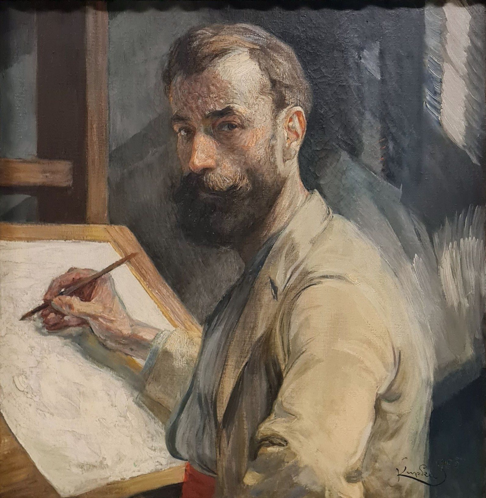 Autorretrato de František Kupka: un hombre con barba, de perfil a tres cuartos, dibuja con un lápiz sobre una lámina apoyada en un tablero.