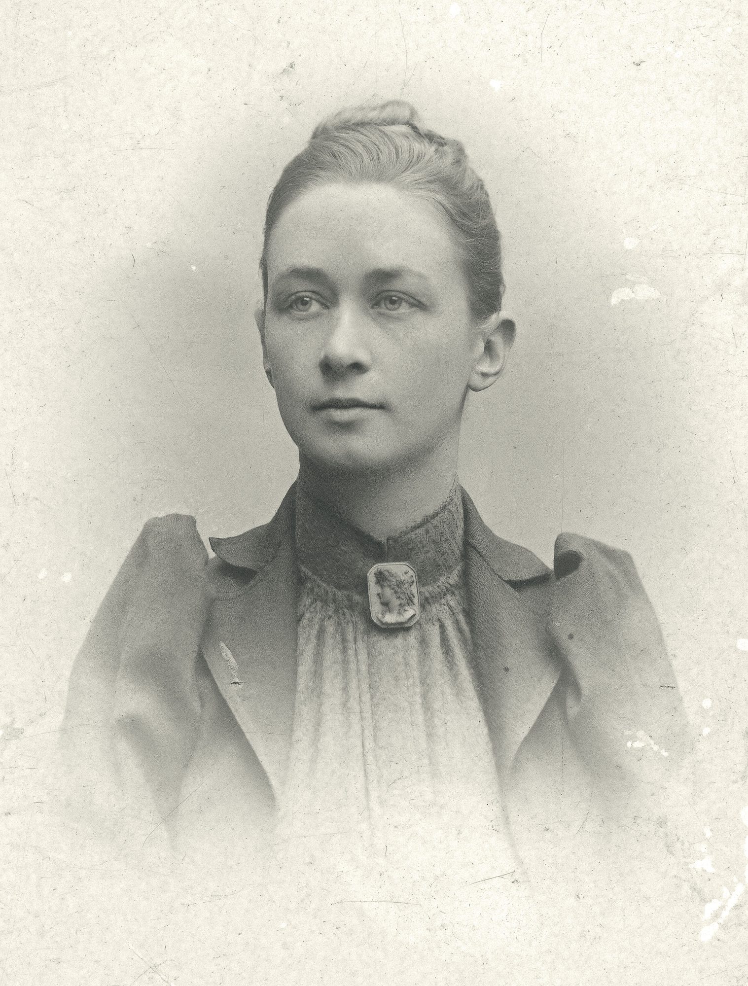 Retrato fotográfico de Hilma af Klint: una mujer joven con el pelo recogido y blusa oscura con broche, mirando a un lado.