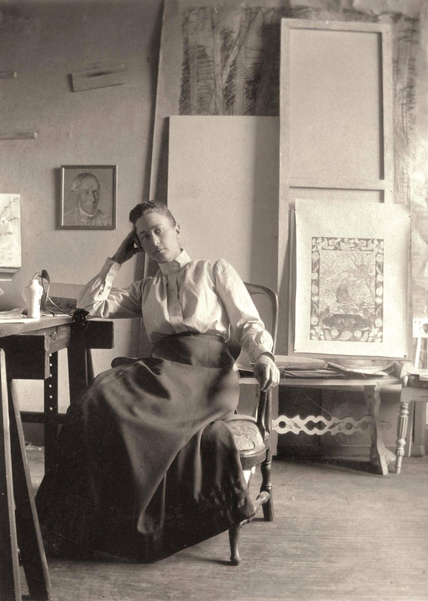 Hilma af Klint sentada en su estudio, con la cabeza apoyada en la mano, rodeada de lienzos y marcos.