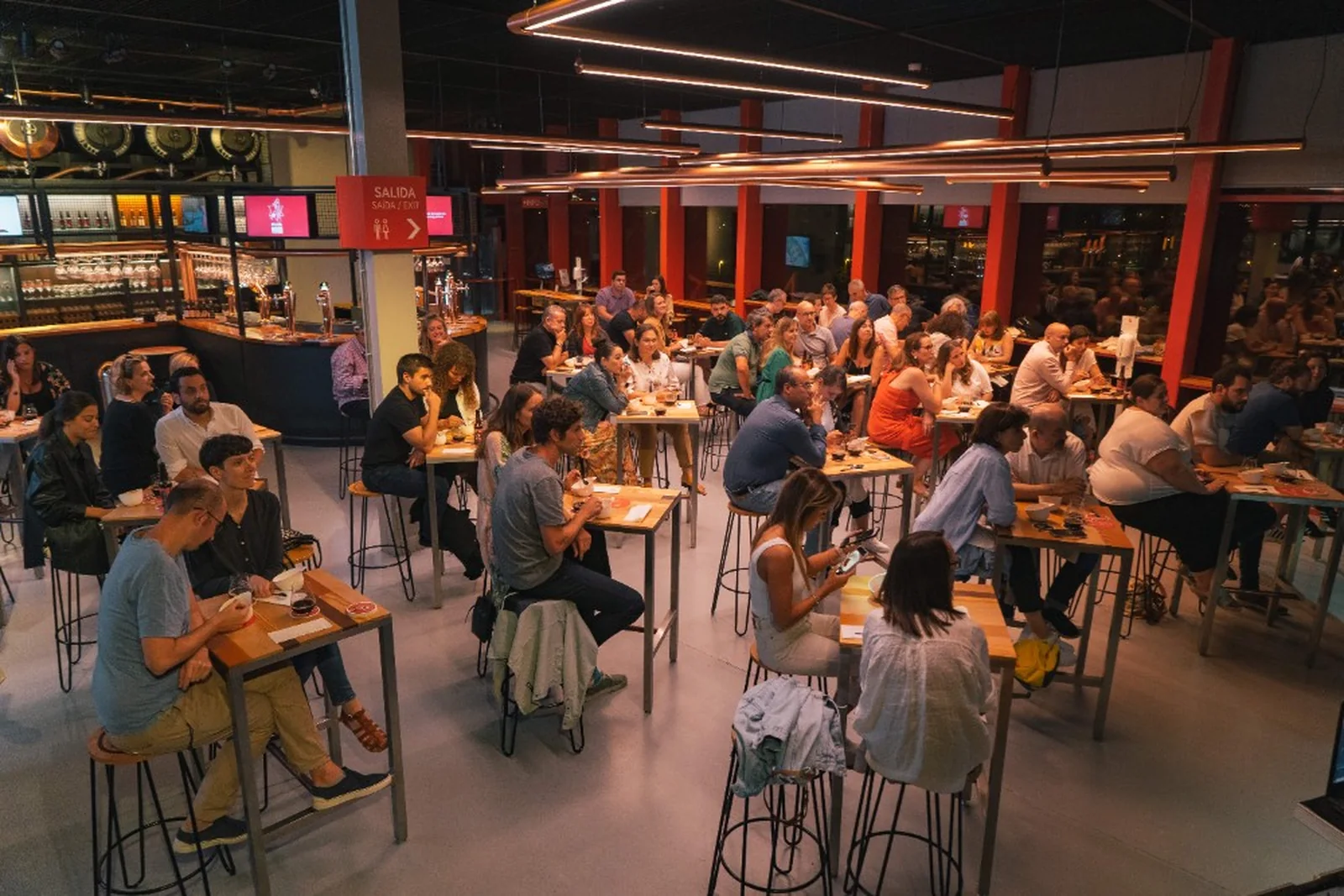 Visitantes sentados alrededor de las mesas de la sala de degustación de MEGA en A Coruña.